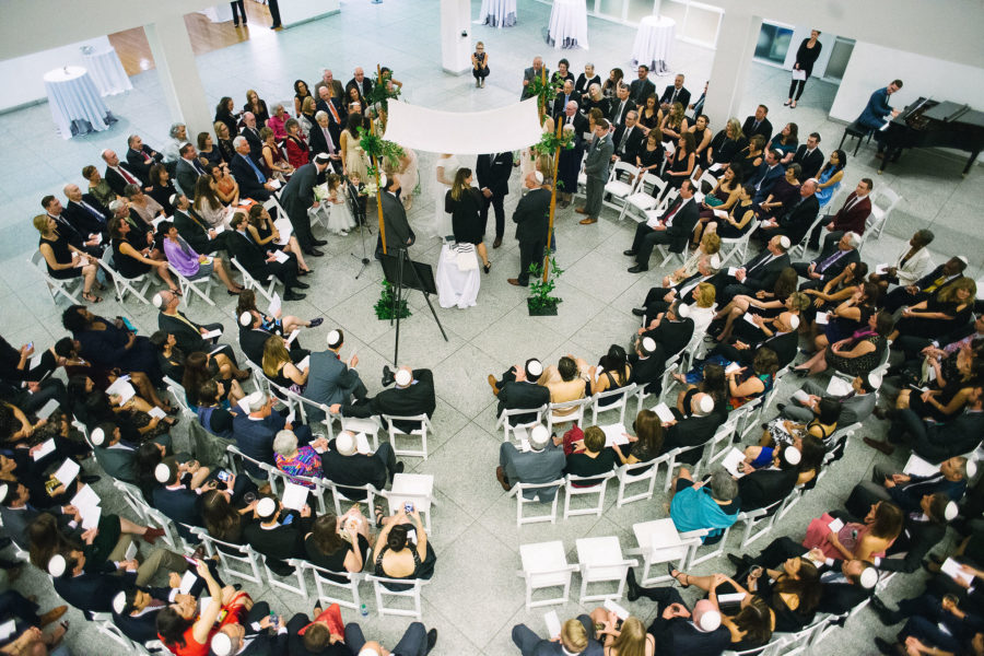 Large group of people in chairs in circle around huppah and couple during wedding ceremony